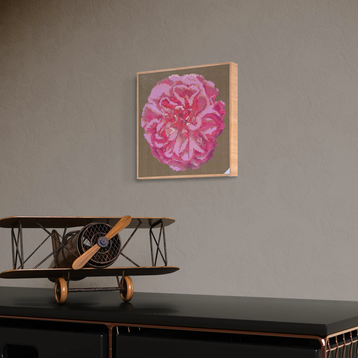 Raumansicht mit Dekorationsobjekten der Micromosaic-Vorlage 'apricot-rose-olive' auf stabilem Buchenholzkörper im Format 25x25x3 cm mit einem eleganten, farblos lackierten Naturholz-Rand. Das Motiv zeigt eine detaillierte Rosenblüte in verschiedenen Rosatönen vor einem monochrom oliv-farbenen Hintergrund. Inspiriert von Garten-Fotos. Das Kunstwerk enthält insgesamt 27 verschiedene Farbnuancen. Perfekt als stilvolle Wanddekoration oder als exklusives Geschenk für Kreative und Kunstliebhaber.