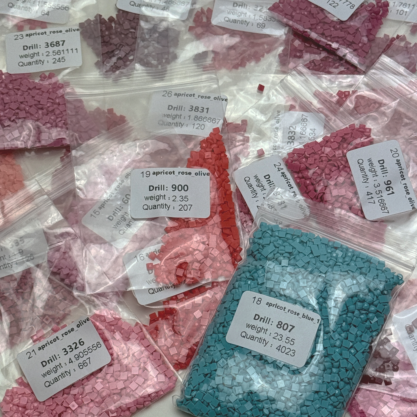 Foto mit Diamond-Painting-Steinchen des Micromosaic Motivs 'apricot-rose-turquoise', abgepackt in Zipper-Tütchen und mit Etiketten versehen, auf denen die Farbnummern gekennzeichnet sind.