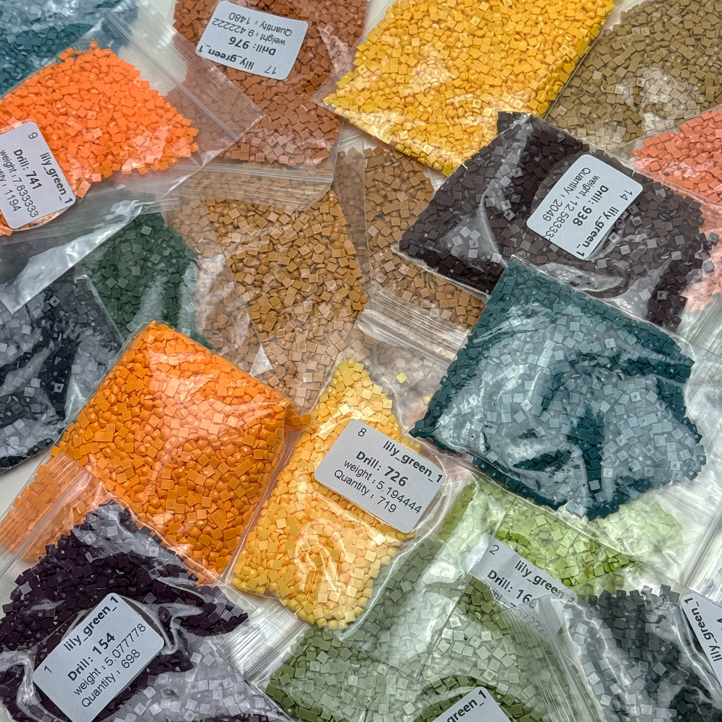 Foto mit Diamond-Painting-Steinchen des Micromosaic Motivs 'lily-green', abgepackt in Zipper-Tütchen und mit Etiketten versehen, auf denen die Farbnummern gekennzeichnet sind.