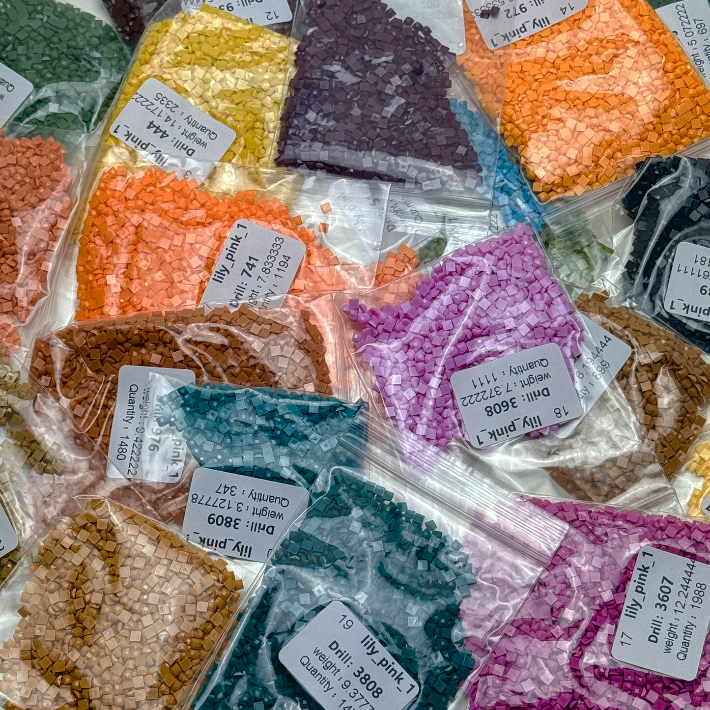 Foto mit Diamond-Painting-Steinchen des Micromosaic Motivs 'lily-pink', abgepackt in Zipper-Tütchen und mit Etiketten versehen, auf denen die Farbnummern gekennzeichnet sind.