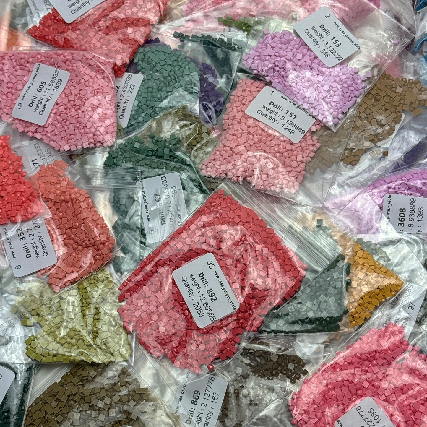 Foto mit Diamond-Painting-Steinchen des Micromosaic Motivs 'rose-violet', abgepackt in Zipper-Tütchen und mit Etiketten versehen, auf denen die Farbnummern gekennzeichnet sind.