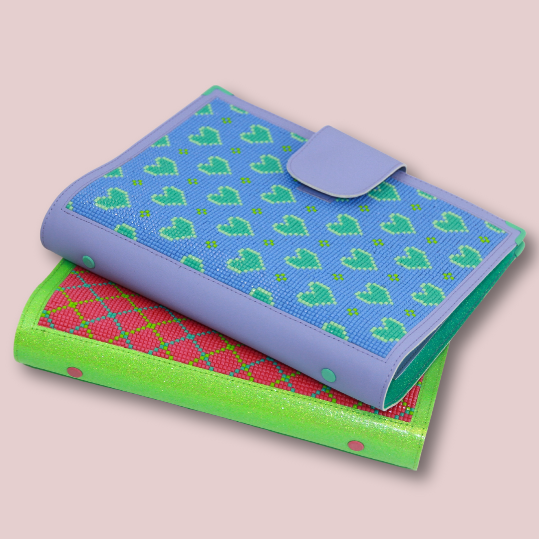 Zwei übereinanderliegende A5-Planer mit Micromosaic-Front: oben ein lila Planer mit Herzmotiv in Blau und Grün, darunter ein grüner Planer mit pink-grünem Rautenmuster, beide auf rosa Hintergrund.
