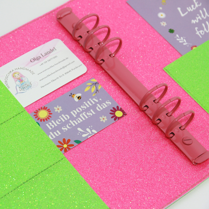 Innenansicht eines genähten A5-Planers mit pink glitzernder Innenseite, pinker Ringmechanik, Visitenkarte von Olga Matroschka Handmade und Motivkarte mit dem Spruch „Bleib positiv, du schaffst das“.